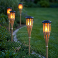 Bamboo solar flame torch lights glowing along a garden path at dusk