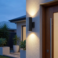 Black up-down LED wall light mounted on an exterior house wall at dusk